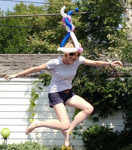 Photo of Heather B. Armstrong mid-air as she jumps on a trampoline wearing a hat sculpted from balloons.